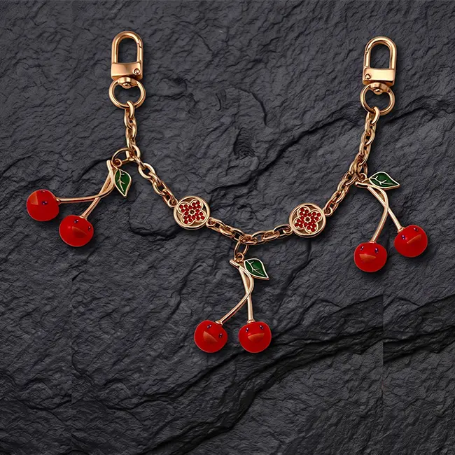 Vista principal de extensores de cadena para bolsos con cerezas de eco-resina roja hojas esmaltadas verdes y motivos florales de pedreria en cadena dorada
