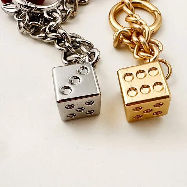 Vista de cerca del ensamblaje enfocada en los dados metalicos en oro claro y plata brillante unidos a las cadenas decorativas