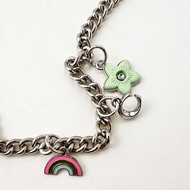Vista de cerca del ensamblaje de herrajes mostrando la flor verde esmaltada y los charms de arcoiris fijados a los eslabones de aleacion de zinc plata