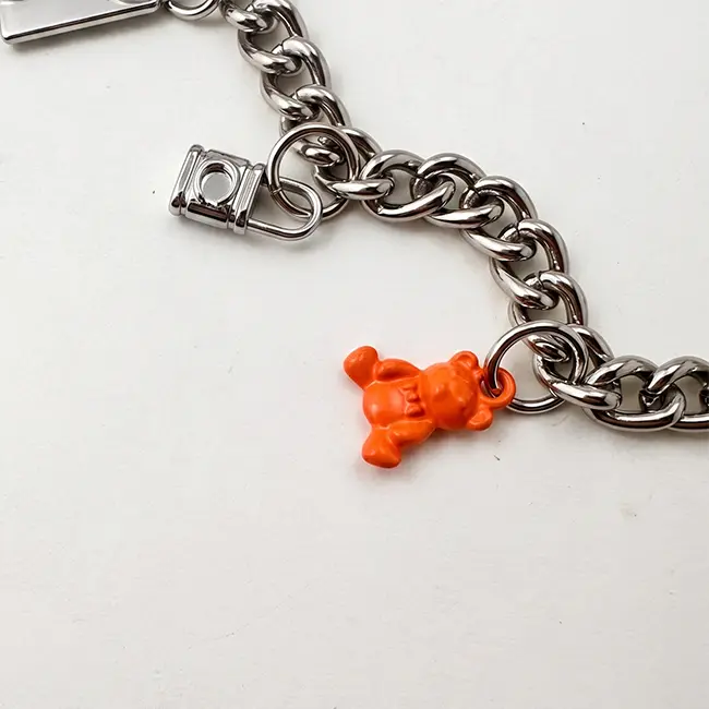 Vista de cerca del ensamblaje enfocada en el osito de eco-resina naranja y el candado en miniatura de metal solido unidos a la cadena de plata