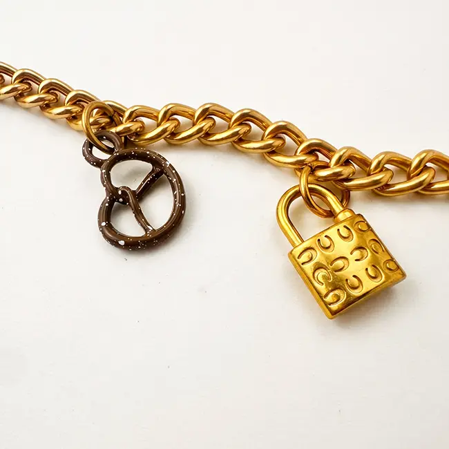 Vista de cerca enfocada en los dijes de metal solido en forma de bolso miniatura y llave esqueleto montados sobre la cadena de eslabones dorados