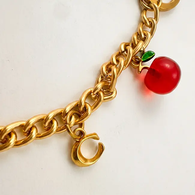 Vista de cerca del ensamblaje enfocada en la manzana de eco-resina roja brillante con detalle de hoja verde fijada a los eslabones dorados