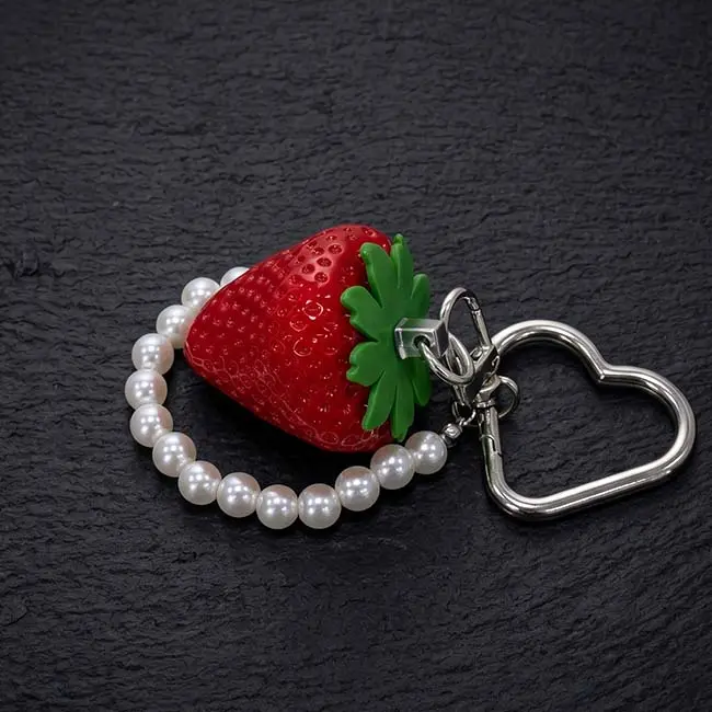 A macro close-up view of the ruby red eco-resin strawberry keyring showing the detailed pitted texture glossy finish green protective calyx moulding and high-strength silver heart clasp assembly on slate.