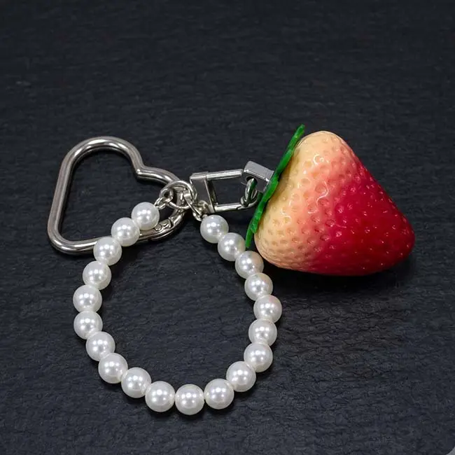 A detailed view of the semi-ripe gradient eco-resin strawberry charm focusing on the realistic yellowish-red transition smooth moulded surface durable metal hardware links and loop of decorative white pearls.