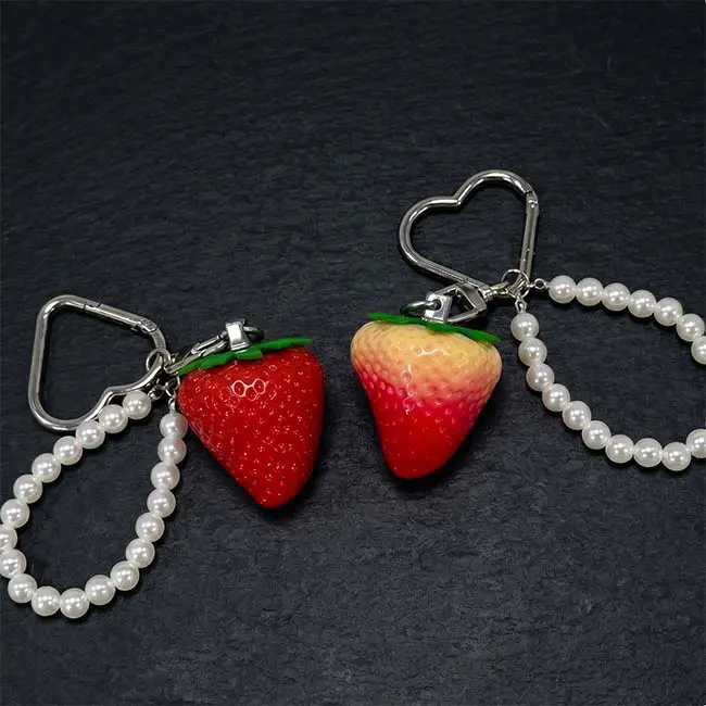 A pair of premium dimensional eco-resin strawberry keyrings in ruby red and semi-ripe gradients featuring polished silver zinc alloy heart-shaped keyrings and elegant white faux pearl loop accent strands.