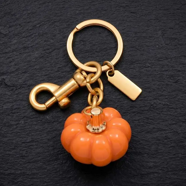 A premium high-gloss orange eco-resin pumpkin keyring component featuring heavy-duty gold-toned zinc alloy hardware including a split keyring a spring snap hook and a customisable blank rectangular brand tag.