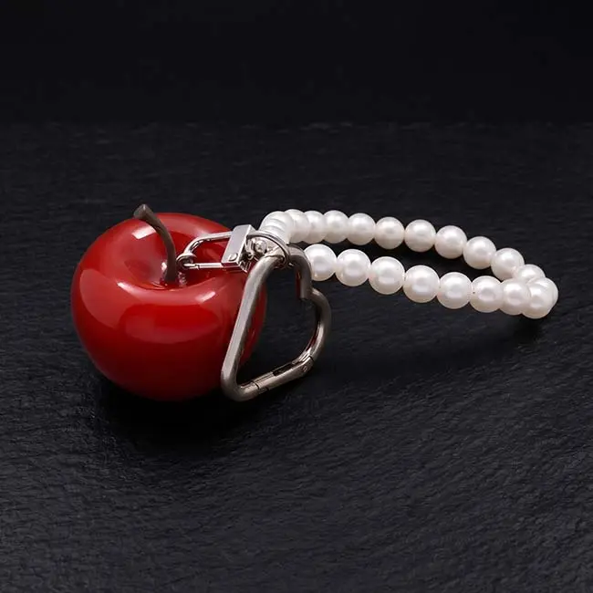 A premium high-gloss red eco-resin apple keyring bag charm featuring a polished silver-toned zinc alloy heart-shaped keyring clasp and a decorative loop accent string of elegant white faux pearls on slate.