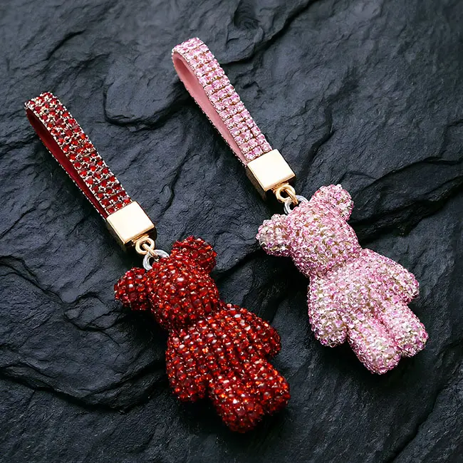 A pair of striking red and pink factory direct pavé charms featuring full body optical rhinestone inlaid bear motifs, complete with matching crystal studded straps and heavy-duty gold tone metal hardware on slate.