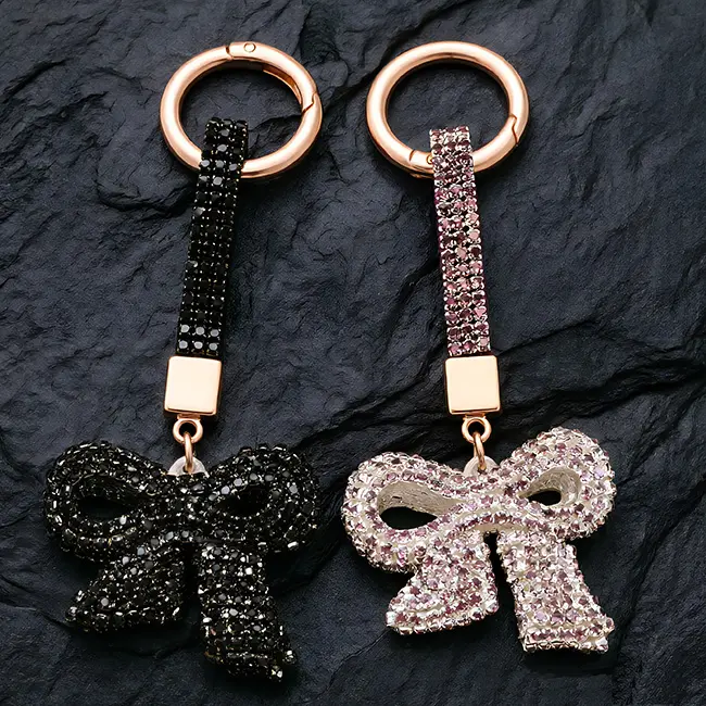 Two factory direct pavé charms full body optical rhinestone inlaid bow motifs in jet black & dusty mauve(purple-pink) highlighting the precise stone setting and robust zinc alloy assembly.
