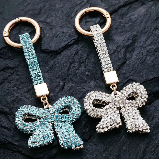A macro material detail view of the aqua blue and crystal clear factory direct pavé charms showcasing the full body optical rhinestone inlaid bow design and brilliant light refraction quality.