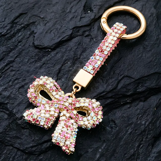A vibrant multi-color rainbow pink with iridescent clear factory direct pavé charms featuring a full body optical rhinestone inlaid bow motif with a matching crystal studded strap on a textured slate background.