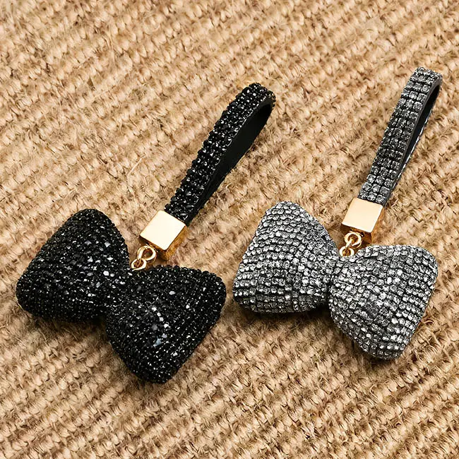 Two factory direct pavé charms featuring full body optical rhinestone inlaid puffy bow motifs in jet black and charcoal gray colors, highlighting the precise stone setting on a textured burlap backdrop.