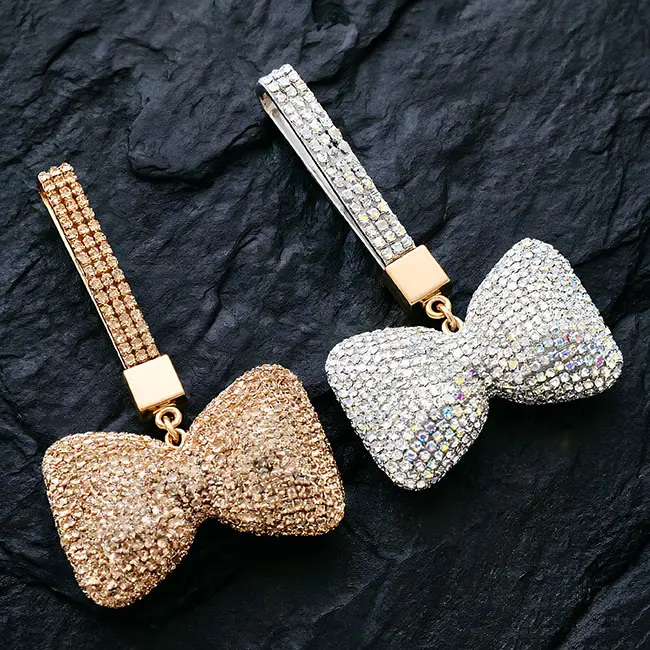 A macro material detail view of the champagne gold and iridescent clear factory direct pavé charms showcasing the full body optical rhinestone inlaid puffy bow design and brilliant light refraction.