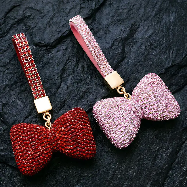 A pair of ruby red and soft pink factory direct pavé charms full body optical rhinestone inlaid puffy bow motifs with matching crystal studded straps and gold hardware on a slate background.