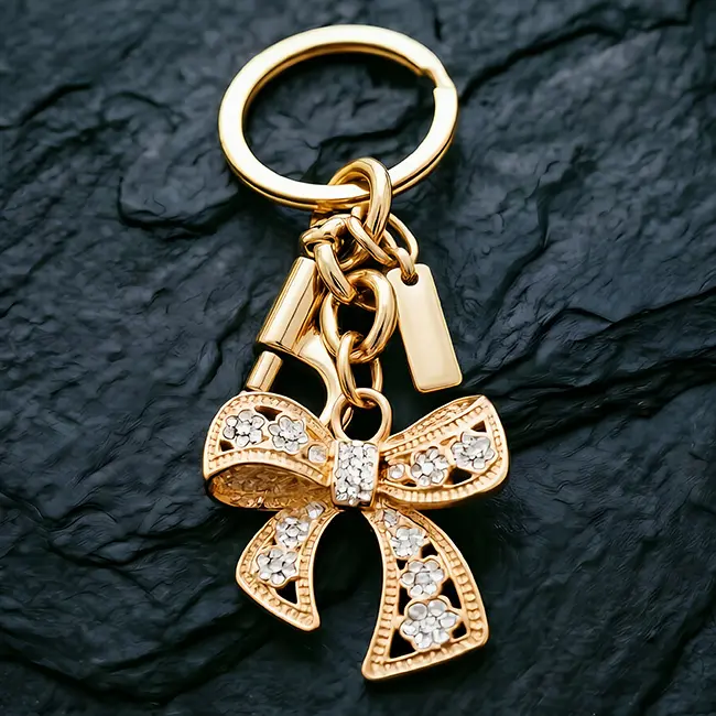 A hardware assembly close up view of the light metallic gold hollow bow custom crystal inlaid components highlighting the brilliant crystal clear optical rhinestones and heavy duty zinc alloy snap hook.
