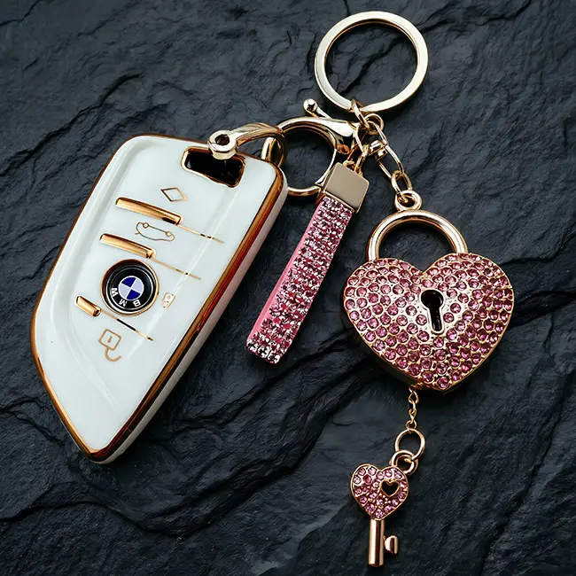 Handheld scale reference view of the light metallic gold heart shape lock custom crystal inlaid components featuring vibrant pink rhinestones placed beside a modern white car key for sizing.