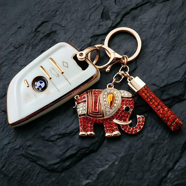 A scale reference view of the custom crystal inlaid components featuring a vibrant ruby red rhinestone elephant with an enamel-infill blanket placed beside a modern white car key to display real world size.