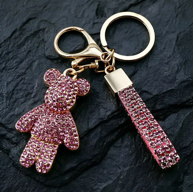 A premium light metallic gold factory direct pavé charms accessory featuring a rose pink optical rhinestone bear with a heavy-duty clasp and a matching crystal studded strap on a dark slate.
