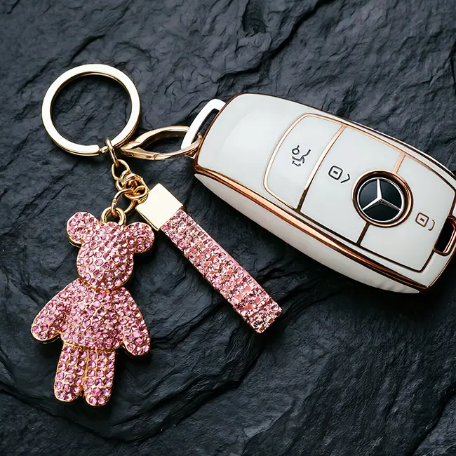 A scale reference view of the factory direct pavé charms featuring a vibrant rose pink rhinestone bear with a matching strap placed beside a modern white car key to display real world size.