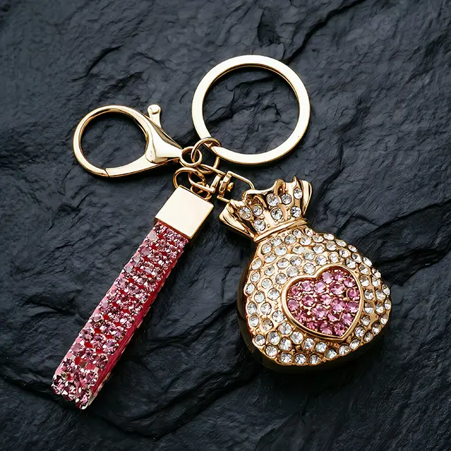 A premium light gold B2B optical crystal molding accessory featuring a rose pink optical rhinestone fortune bag charm with a heavy-duty clasp and matching crystal studded strap on a dark slate.