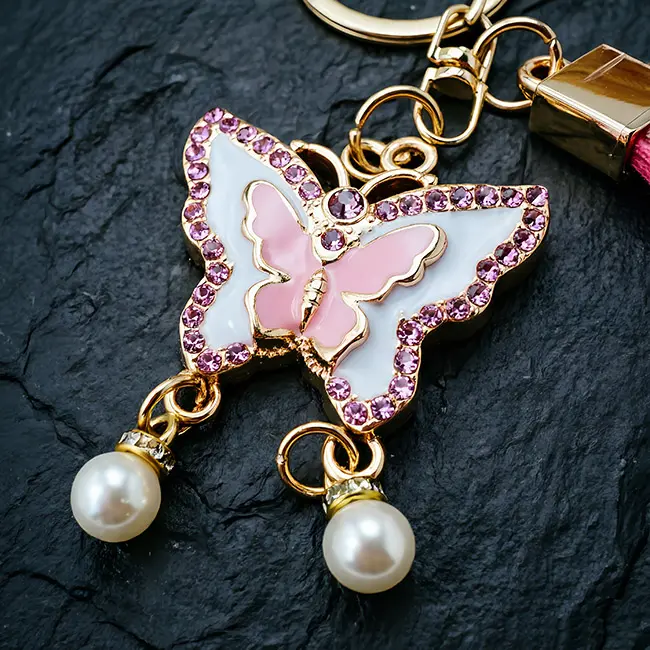 A macro material detail view of the wholesale rhinestone keychains showcasing the soft pink enamel butterfly charm, highlighting the precise pink optical rhinestone edges and delicate pearl dangles.