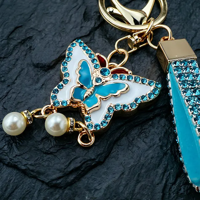 Close up view of the wholesale rhinestone keychains highlighting the vibrant teal blue enamel butterfly charm, brilliant blue optical rhinestone edges,heavy duty clasp and delicate pearl dangles.