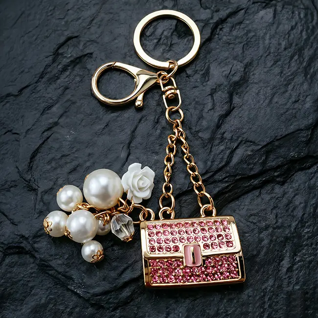 A premium light gold enamel B2B optical crystal molding accessory featuring a rose pink optical rhinestone fortune purse charm with a delicate flower bud and elegant simulated pearl dangles on slate.