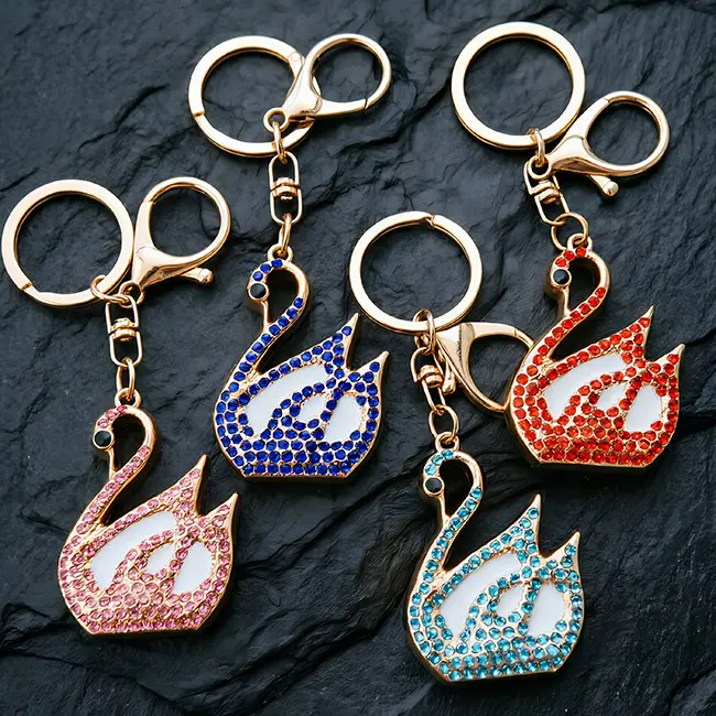 A macro material detail view of the B2B optical crystal molding keychain showcasing four vibrant goose charms in ruby red, cobalt blue, soft pink, and teal blue rhinestones with pristine white enamel.