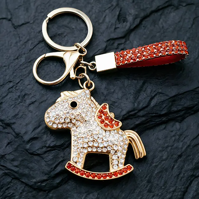 A premium light gold bulk crystal hardware accessory featuring an orange-red optical rhinestone rocker horse with a gold ingot, complete with standard assembly clasp and strap on a dark mat.