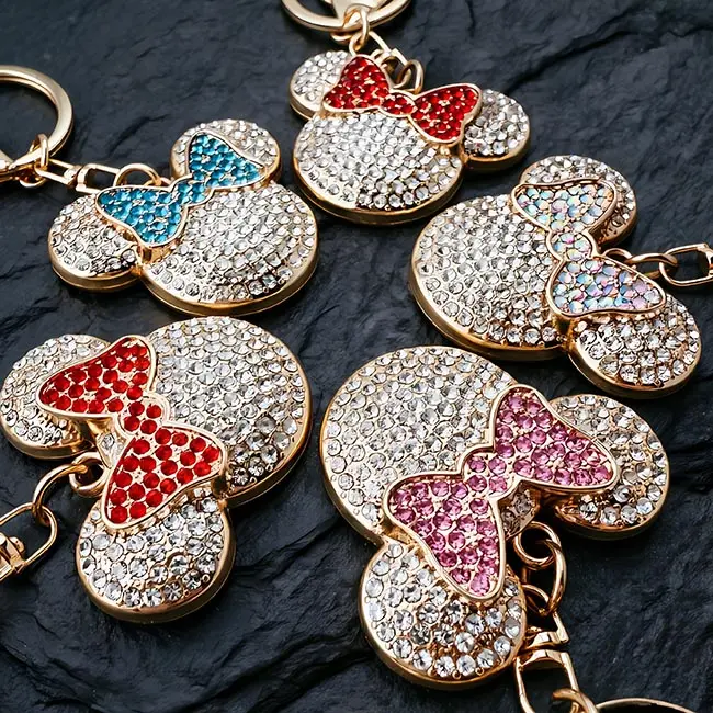 A macro material detail view of the B2B optical crystal molding keychain showcasing four vibrant mouse head charms highlighting precise ruby red, teal blue, soft pink, and iridescent clear bows.