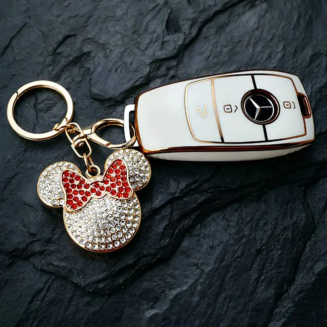 A scale reference view of the B2B optical crystal molding accessory featuring a ruby red rhinestone mouse head charm with a heavy duty clasp placed next to a modern luxury white vehicle key for accurate sizing.
