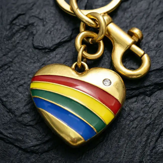 A macro material detail view of the wholesale zinc alloy keyrings showcasing the precision die-cast rainbow heart motif - vibrant glossy enamel-infill stripes - sparkling optical rhinestone - and gold metal hardware.