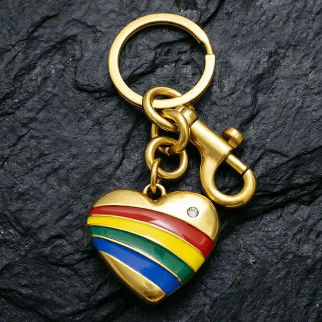 A premium enamel-infill rainbow heart motif component serving as high-end wholesale zinc alloy keyrings - featuring vibrant colour stripes - an optical rhinestone inlay - and a heavy-duty gold-toned snap hook on slate.