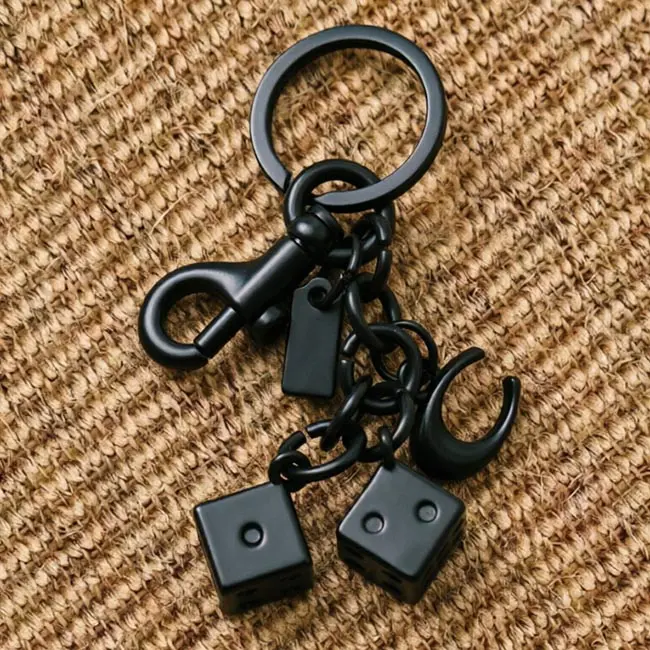 A matte black precision die casting keyrings dice component featuring two solid zinc alloy dice charms an uppercase C accent a heavy duty spring snap hook and a blank custom logo tag on a woven mat.