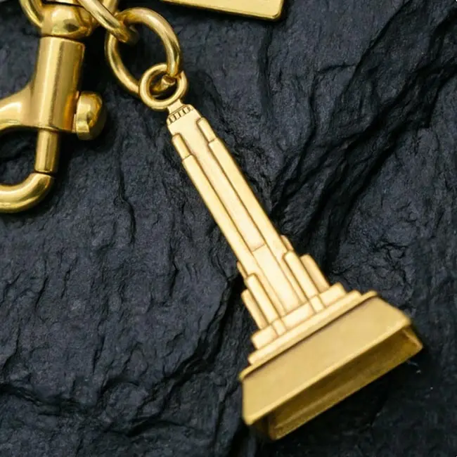 A macro material detail view of the gold bulk 3D moulded charms showcasing the precision die-cast iron tower setbacks - structural details - and radiant gold plating over high-grade zinc alloy.