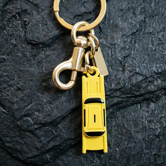 A macro material detail view of the yellow bulk 3D moulded enamel infill charms taxi keyring highlighting the precision die-cast car body - vibrant industrial enamel paint finish - and heavy-duty metal links.