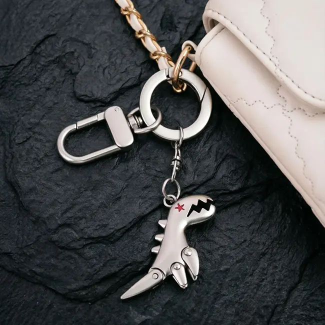 A macro detail view of the silver dinosaur wholesale Precision Zinc Alloy Castings keyring attached to a white quilted bag - highlighting the precision die-cast body and heavy-duty zinc alloy metal links.