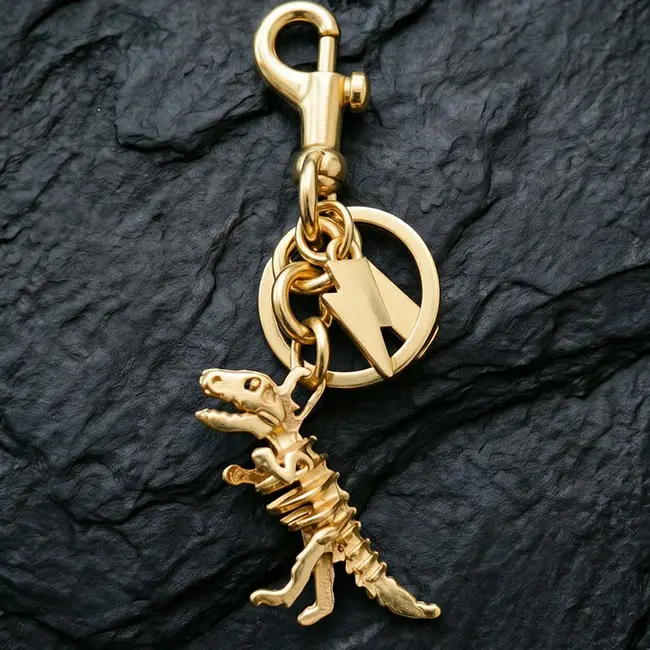 A premium gold T-Rex skeleton Precision Zinc Alloy 3D moulded charms component featuring a solid metal dinosaur bone charm - a lightning bolt tag - a spring snap hook - and durable hardware links.