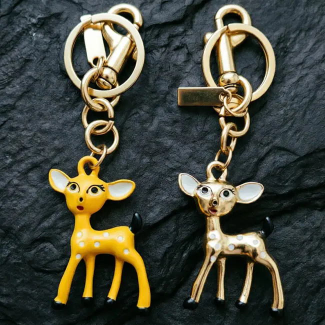 A pair of premium enamel infill Sika deer Precision Zinc Alloy 3D moulded charms featuring vibrant yellow and metallic gold fawns heavy duty spring snap hooks and blank tags on a slate mat