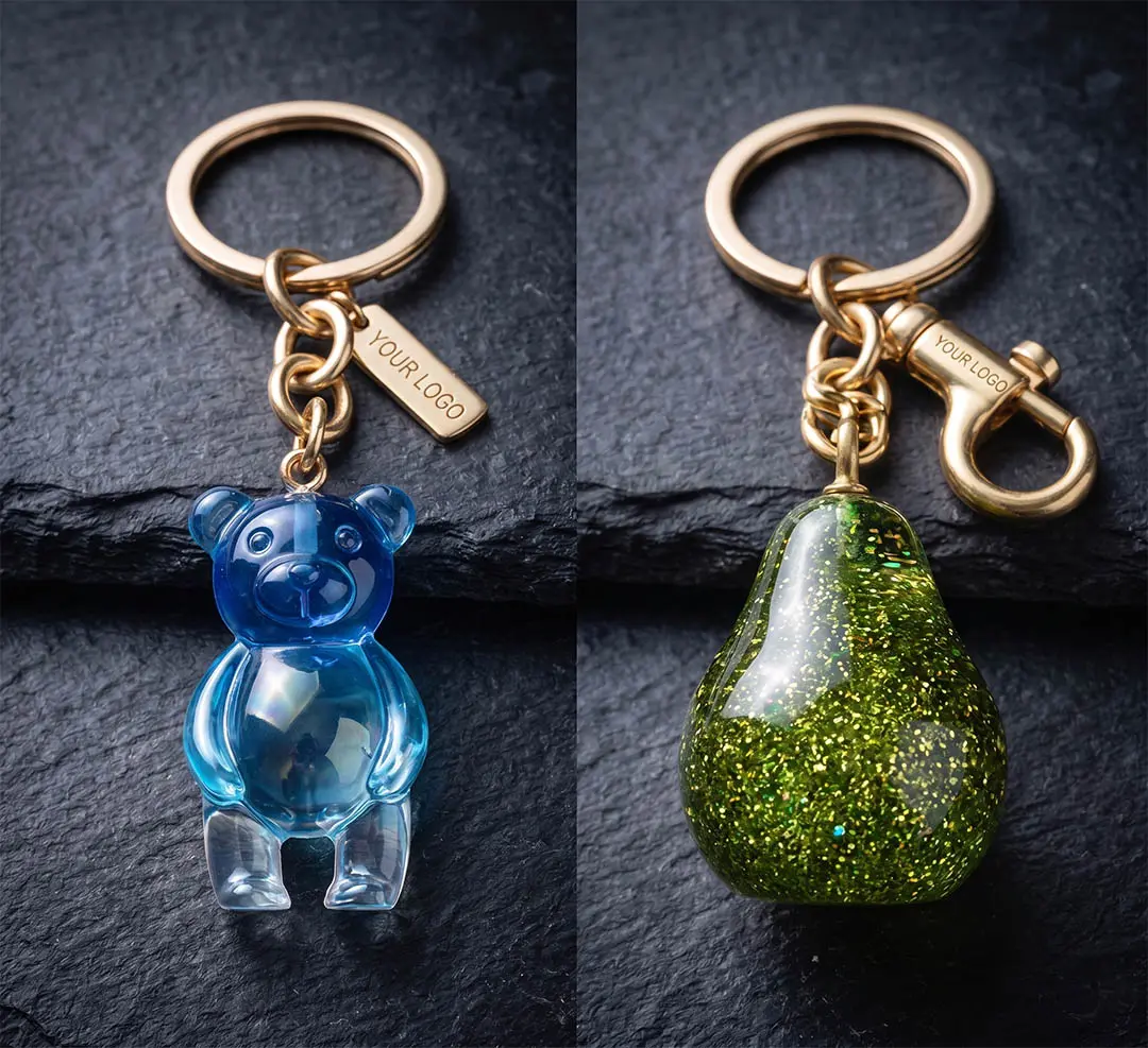 Macro product photography of custom keychains featuring advanced translucent blue resin casting with subtle gradients and a green pear shape with suspended fine glitter particles, proving bespoke hardware suspension capabilities.